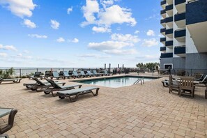 A poolside area with lounge chairs and a pool, surrounded by a building with balconies. - Renovated Condo with Gorgeous Ocean Views (Myrtle Beach)
