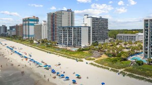 A beachfront hotel with multiple high-rise buildings, a sandy beach with umbrellas, and a swimming pool. - Renovated Condo with Gorgeous Ocean Views (Myrtle Beach)