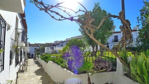 A courtyard with a stone pathway, potted plants, and a tree with a nest. - R1358 | La Hacienda 10 | Burriana (Nerja)