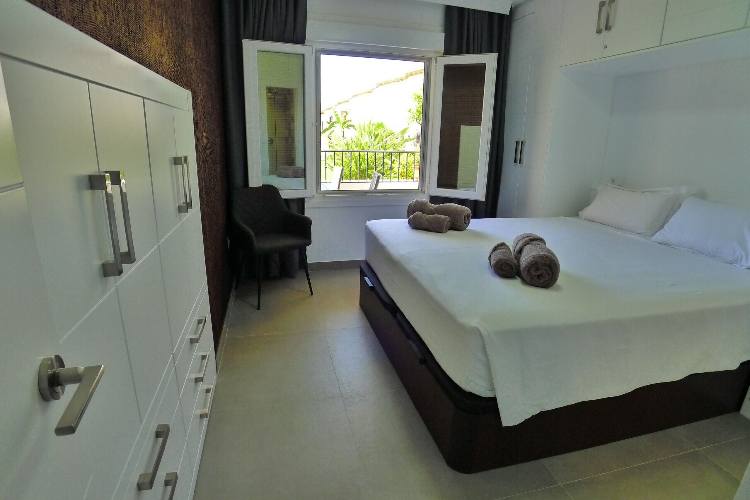 A hotel room with a bed, a chair, a desk, and a window with a view of greenery.
