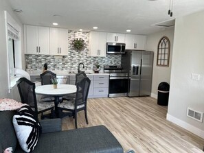 Una cocina moderna con armarios blancos, un refrigerador de acero inoxidable y un microondas. Hay una zona de comedor con una mesa redonda y sillas.