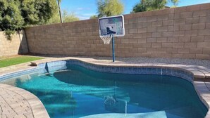 Ein Schwimmbecken mit einem Basketballkorb und einer Ziegelwand im Hintergrund.