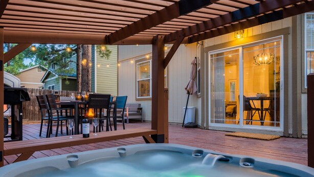 A hot tub in a covered outdoor area with a wooden deck, a dining table with chairs, and a patio umbrella.