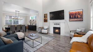 A modern living room with a fireplace, a dining area, and a TV mounted on the wall.