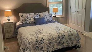 Um quarto com uma cama, duas mesas de cabeceira com abajures, uma janela e uma porta.