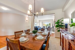 Ein Essbereich mit einem Holztisch, gedeckt für vier Personen, umgeben von Holzstühlen. Über dem Tisch hängt eine Chandelier, und auf der rechten Seite ist ein Blumentopf zu sehen.