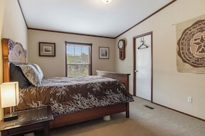 Um quarto com cama, mesa de cabeceira, relógio na parede, janela e porta.