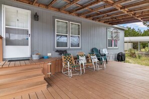 Eine überdachte Terrasse mit einer Holztreppe, Sitzgelegenheiten im Freien mit gemusterten Stühlen und einem Grillbereich.