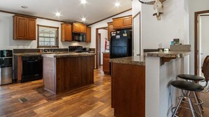 A kitchen with wooden cabinets, a black refrigerator, a microwave, and a stove. - Hondo Creek Hideaway (Tarpley)