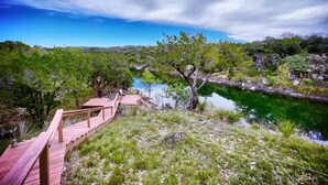 A wooden deck leading to a natural landscape with a lake and trees. - Hondo Creek Hideaway (Tarpley)