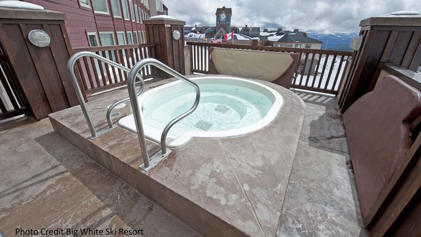 A hot tub on a balcony with a view of a town and mountains. - Whitefoot Lodge Studio in Village Centre (Beaverdell)