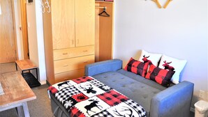 A bedroom with a bed, a wardrobe, a table, and a bench. - Whitefoot Lodge Studio in Village Centre (Beaverdell)