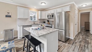 A modern kitchen with white cabinetry, stainless steel appliances, and a marble island.