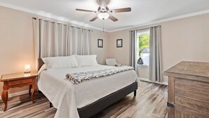 A bedroom with a bed, a nightstand, a ceiling fan, and a view of the outdoors.