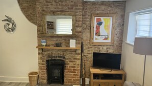 Una sala de estar con chimenea de ladrillo, un televisor sobre un soporte de madera, una cesta de mimbre y un cuadro en la pared.