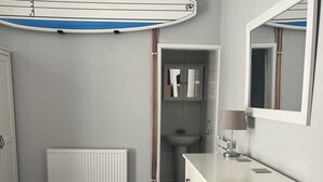 Un dormitorio con cama, cómoda, silla, espejo y una tabla de surf colgada en la pared.