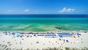 A beach with rows of blue and white sunbeds and umbrellas, a clear blue sky, and calm turquoise waters.