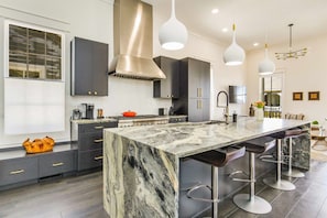 A modern kitchen with a large island, dark cabinets, and pendant lighting.