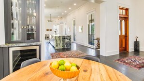 A modern kitchen with a marble island, a dining area with a wooden table and a bowl of fruit, and a view into the living area. - Downtown Pensacola Historic Home (pensacola)