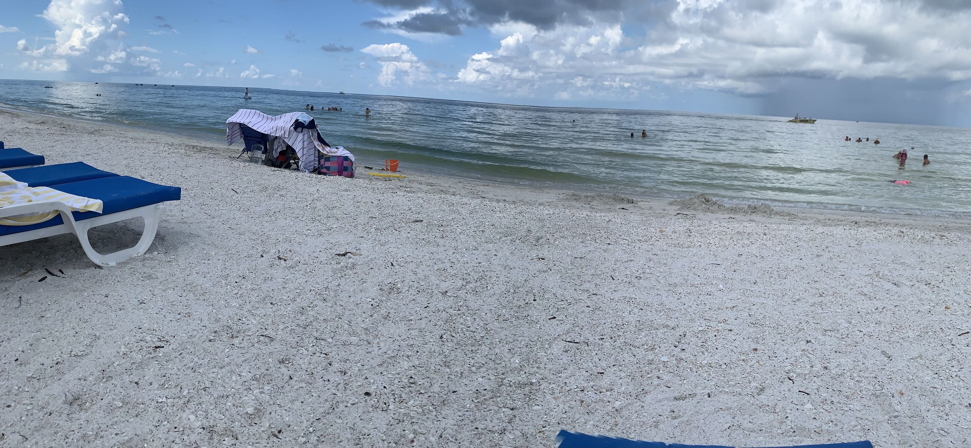 A beach with white sand, a few beach chairs, and a covered area with a table and chairs.