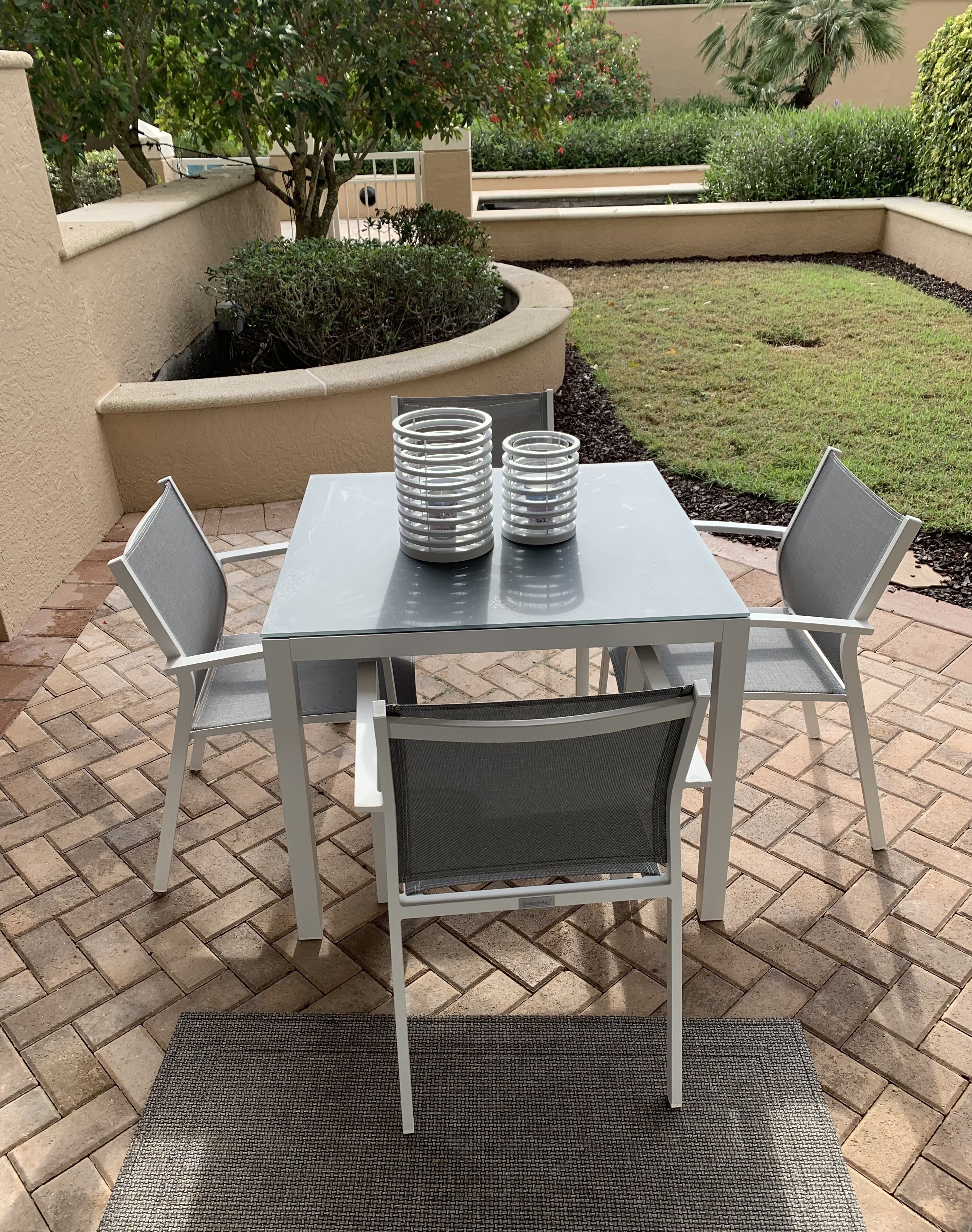 An outdoor patio with a table and chairs, surrounded by a brick floor and a small garden area.