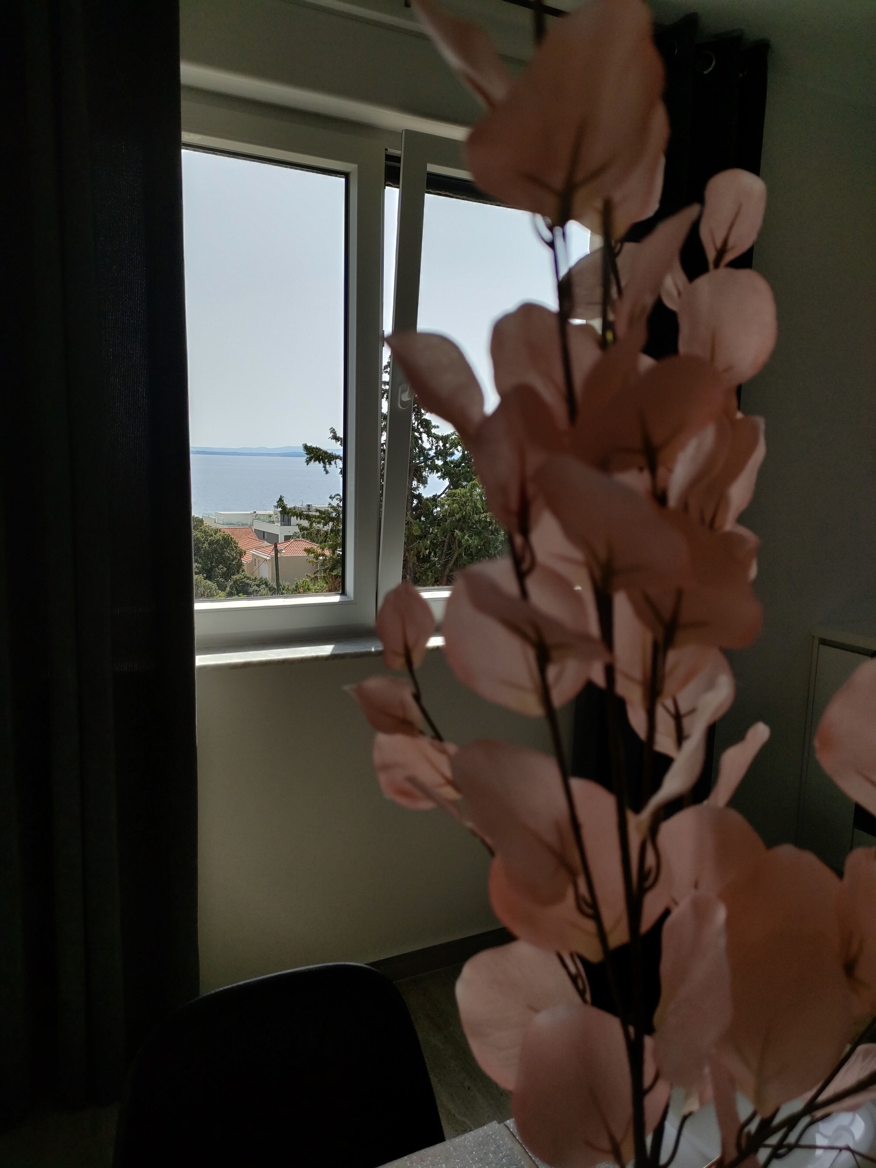 A room with a view of the sea through a window, a chair, and a table.