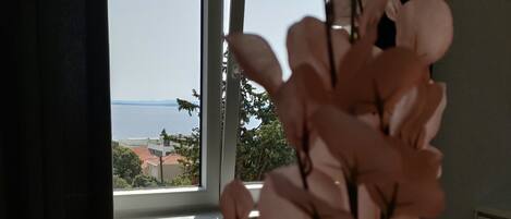 A room with a view of the sea through a window, a chair, and a table.