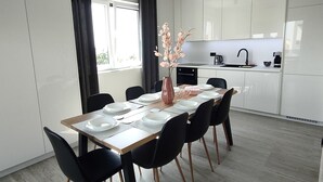Una cocina moderna con armarios blancos, una zona de comedor con una mesa de madera y sillas negras, y un jarrón con flores rosas sobre la mesa.