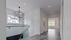 Un intérieur moderne avec un escalier, un luminaire au plafond aux motifs géométriques et une vue sur l’extérieur.