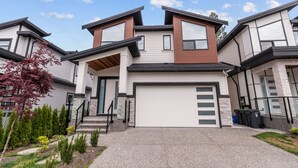 Une maison moderne à deux étages, dotée d’un garage, de fondations en pierre et d’un jardin paysager à l’avant.