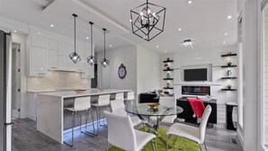 Une cuisine moderne avec des meubles blancs, un îlot central doté de tabourets et des luminaires suspendus.