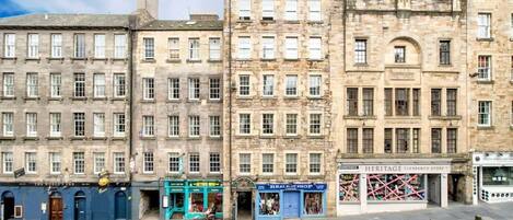 A row of historic stone buildings with shops on the ground floor, including a heritage store and a real estate shop.