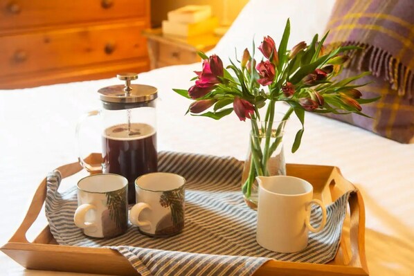 A tray with coffee-making equipment and mugs on a bed.