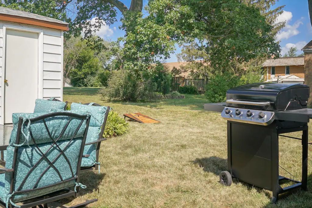 A backyard with a grill, a covered seating area, and a shed.