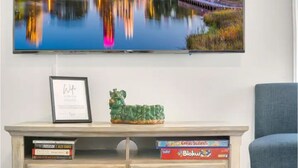 Olohuoneessa on seinälle asennettu taulutelevisio, kehystetty todistus puukalusteessa ja pieni vihreä koristehahmo.
