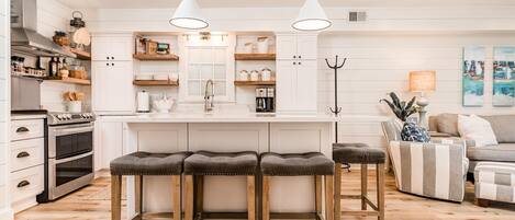 A modern kitchen with white cabinetry, a central island with stools, and a dining area with a sofa and a lamp.