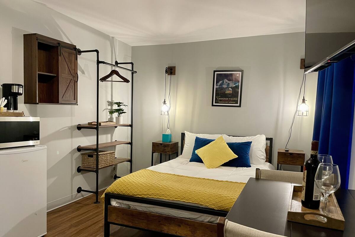 Ein Hotelzimmer mit Bett, Nachttischen, einem Schreibtisch, einer Pendelleuchte, einem Wandregal und einem Poster.
