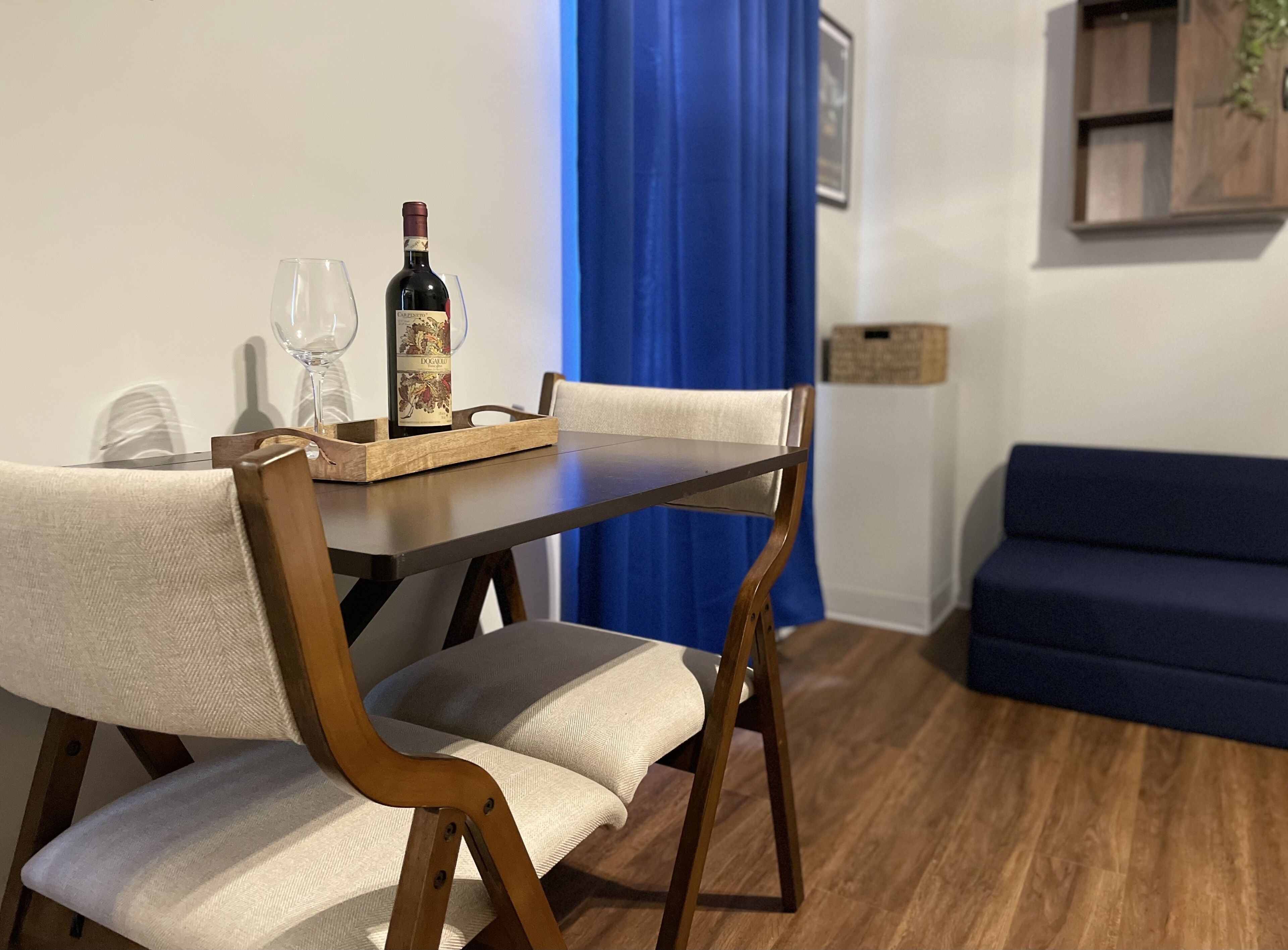 Un comedor con mesa de madera, dos sillas, una botella de vino y copas.