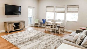 Ein Wohnzimmer mit Flachbildfernseher, einem Esstisch mit Stühlen, einer Couch und einem großen Teppich.