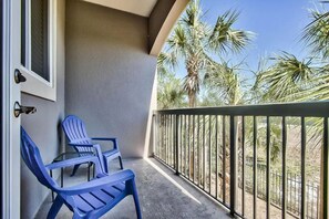 Enjoy the serene view of palm trees from this balcony, featuring two comfortable chairs and a small table.