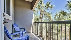 Ein Balkon mit zwei blauen Stühlen und einem Glastisch, mit Blick auf Palmen und einen klaren Himmel.