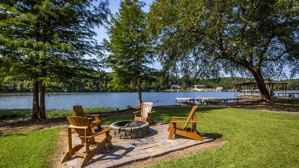 Eine Uferterrasse mit Adirondack-Stühlen, einer Feuerstelle und einem Pavillon mit Blick auf das Wasser.