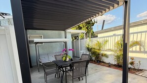 Una zona de pati coberta amb taula i cadires, una barbacoa i plantes en testos.