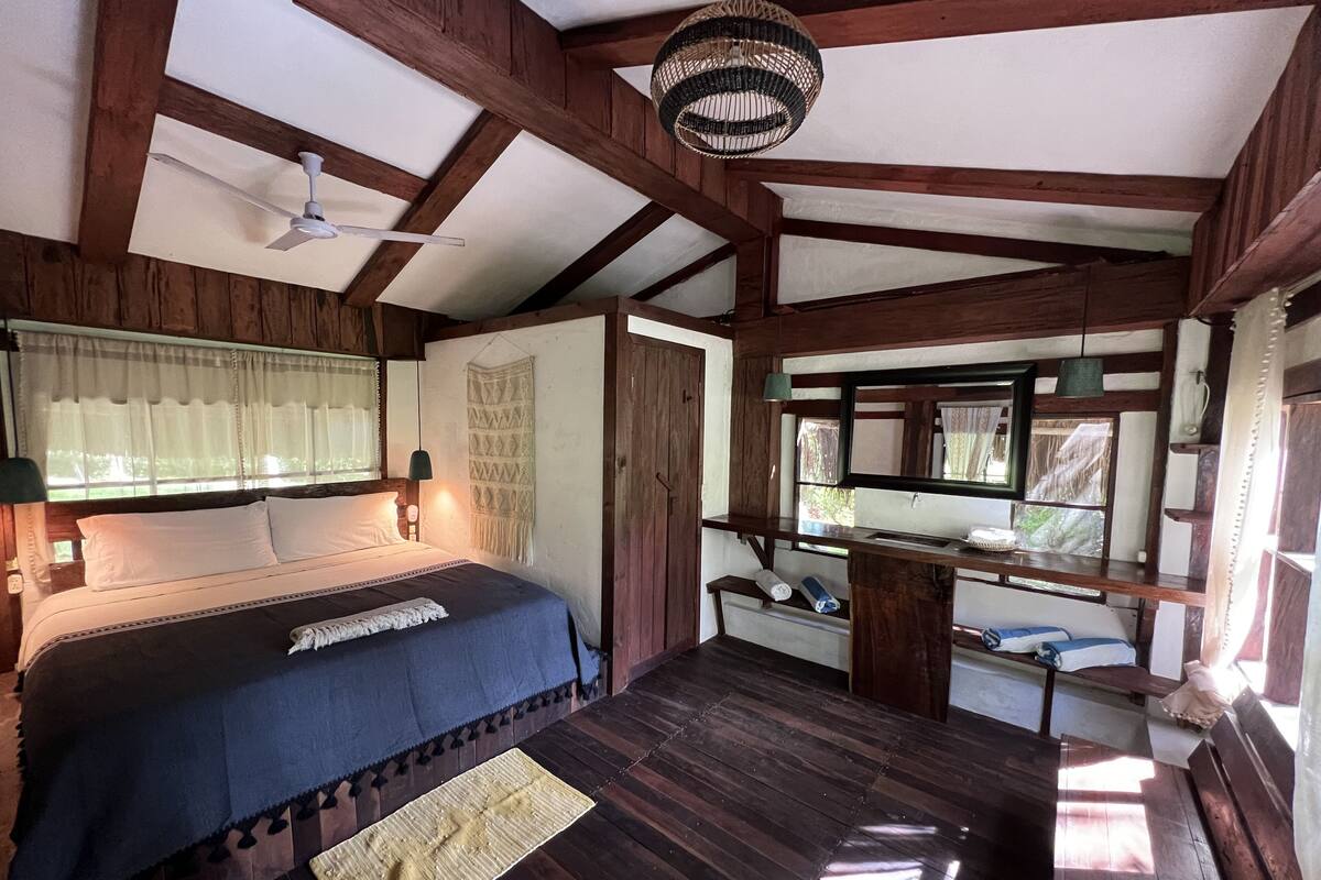 A bedroom with a bed, a desk, a mirror, and a ceiling fan.