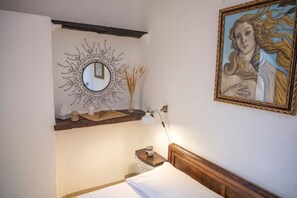 Une chambre à coucher comprenant un lit, une table de chevet, un miroir fixé au mur, une étagère avec des objets décoratifs et un tableau.