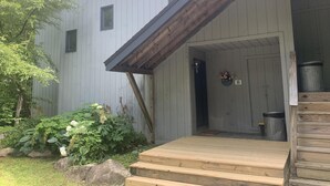 Un bâtiment en bois doté d’un porche, d’une porte et d’un petit jardin agrémenté de plantes et de rochers.