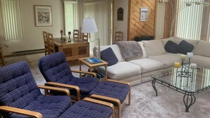 Un salon chaleureux avec un canapé, deux fauteuils, une table basse en verre et une table à manger en bois avec des chaises.