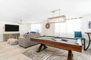 Uma sala de estar moderna com mesa de bilhar, um sofá, uma televisão e um espelho decorativo.