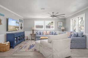 Ein Wohnzimmer mit großem Fenster, Deckenventilator, blauem Schrank und Fernseher an der Wand.