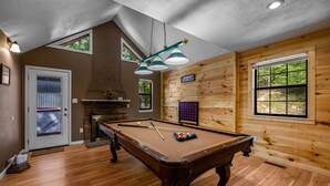 A pool table with a billiard cue, balls, and a rack in a room with wooden walls, a fireplace, and a sign indicating a play room. - Hot Tub, Game Room, Pool Table, Fireplace | Minutes to Pigeon Forge (Sevierville)